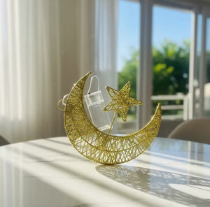 Decorative gold moon and star ornament on a reflective surface with a blurred outdoor background